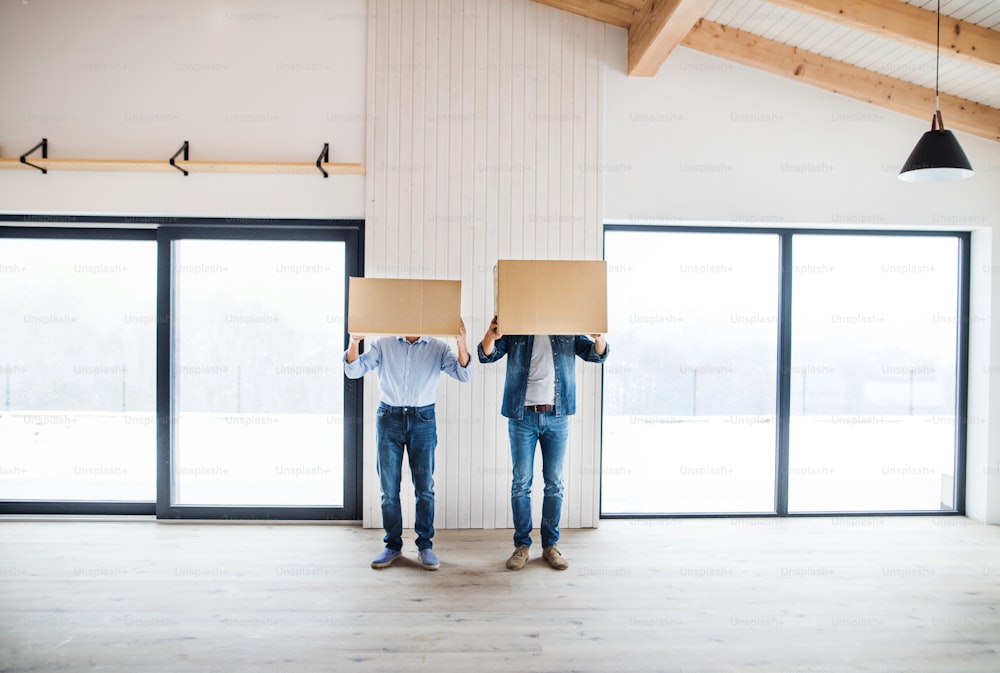 Due uomini che tengono scatole di cartone davanti alla loro testa quando arredano una nuova casa, un nuovo concetto di casa.