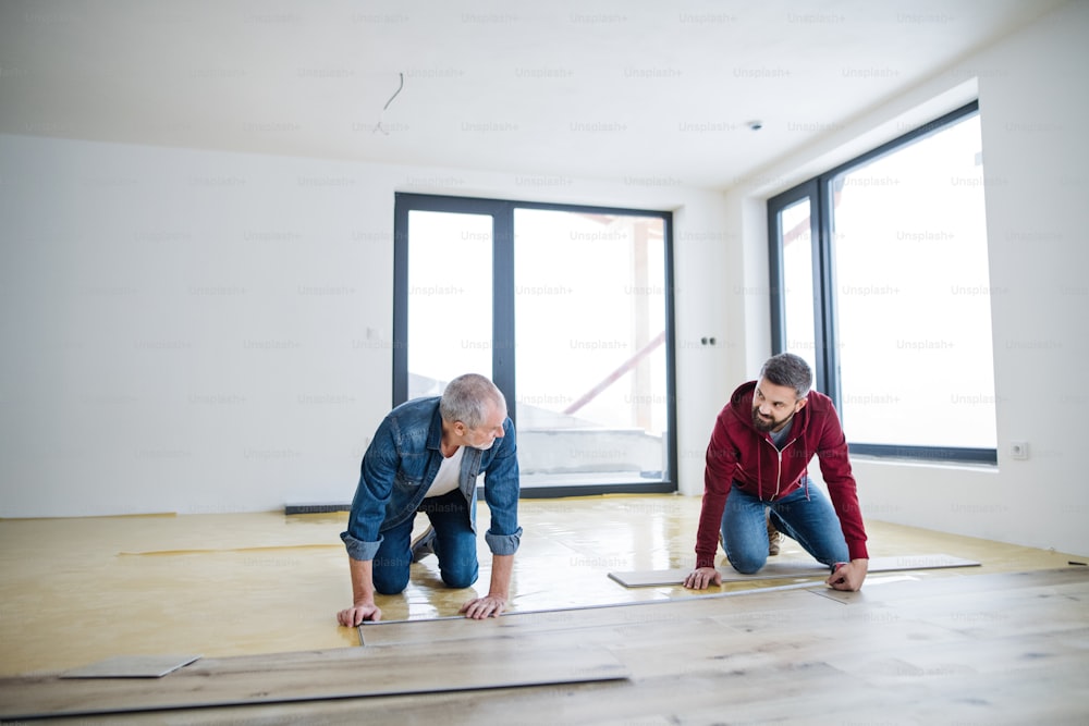 A front view of mature man with his senior father laying wood flooring, a new home concept.