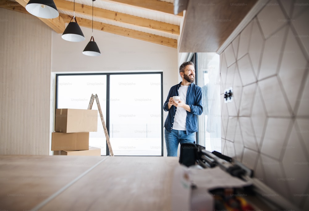 A mature man with cardboard boxes and cup of coffee standing by a window, furnishing new house. A new home concept. Copy space.