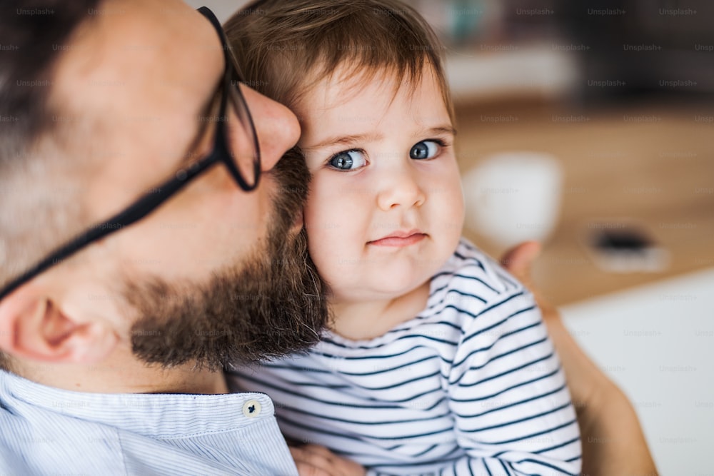 A close-up portrait of mature father with a toddler girl indoors, kissing.