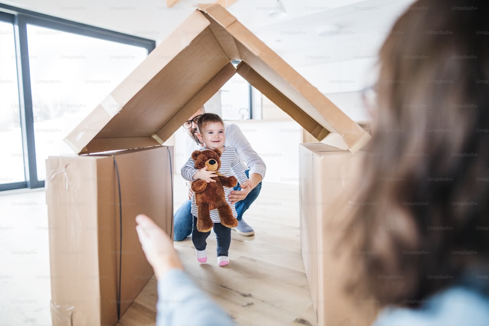 Uma jovem família com uma criança feliz dentro de casa, movendo-se em um novo conceito de casa.