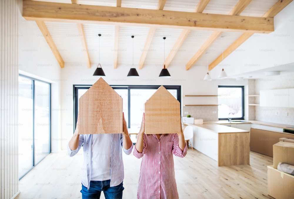 Una pareja joven cubriendo rostros con casa de madera. Un concepto de mudanza en un nuevo hogar. Espacio de copia.
