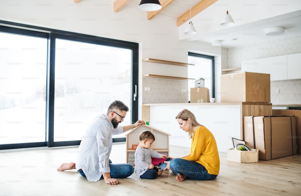Un retrato de una familia joven feliz con una niña pequeña que se muda a una nueva casa, jugando.