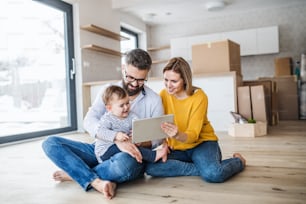 A young family with a toddler girl sitting barefooton the floor when moving in new home, using tablet.