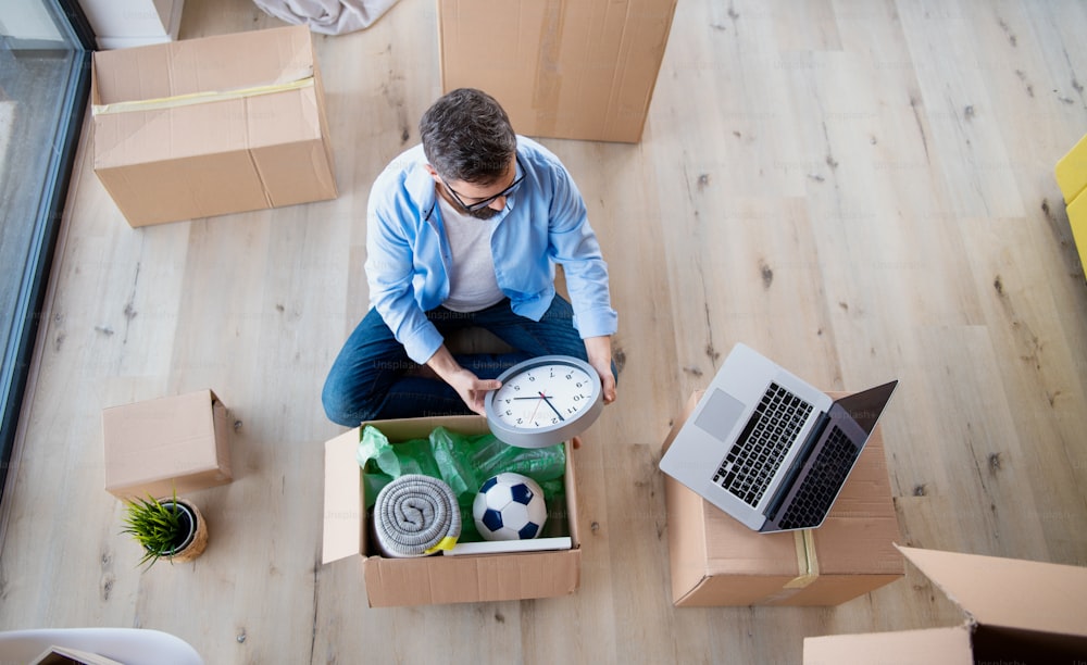 Vista superior de un hombre maduro con cajas moviéndose en una casa nueva, sentado y desempacando.