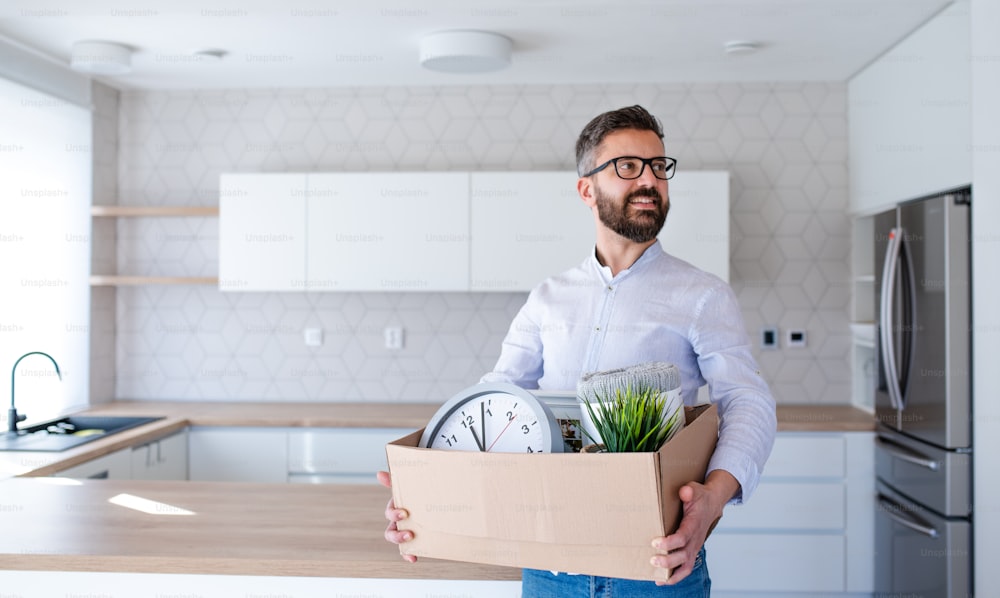 Un hombre maduro parado en una casa sin amueblar, sosteniendo una caja. Un concepto de mudanza en un nuevo hogar.