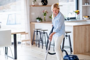 Portrait of happy senior woman with vacuum cleaner indoors at home, hoovering.