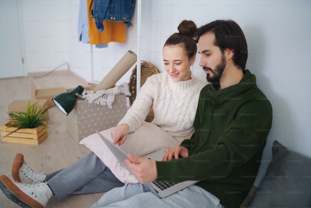 Feliz pareja joven con computadora portátil y cajas que se mudan en un nuevo piso, un nuevo hogar y un concepto de reubicación.