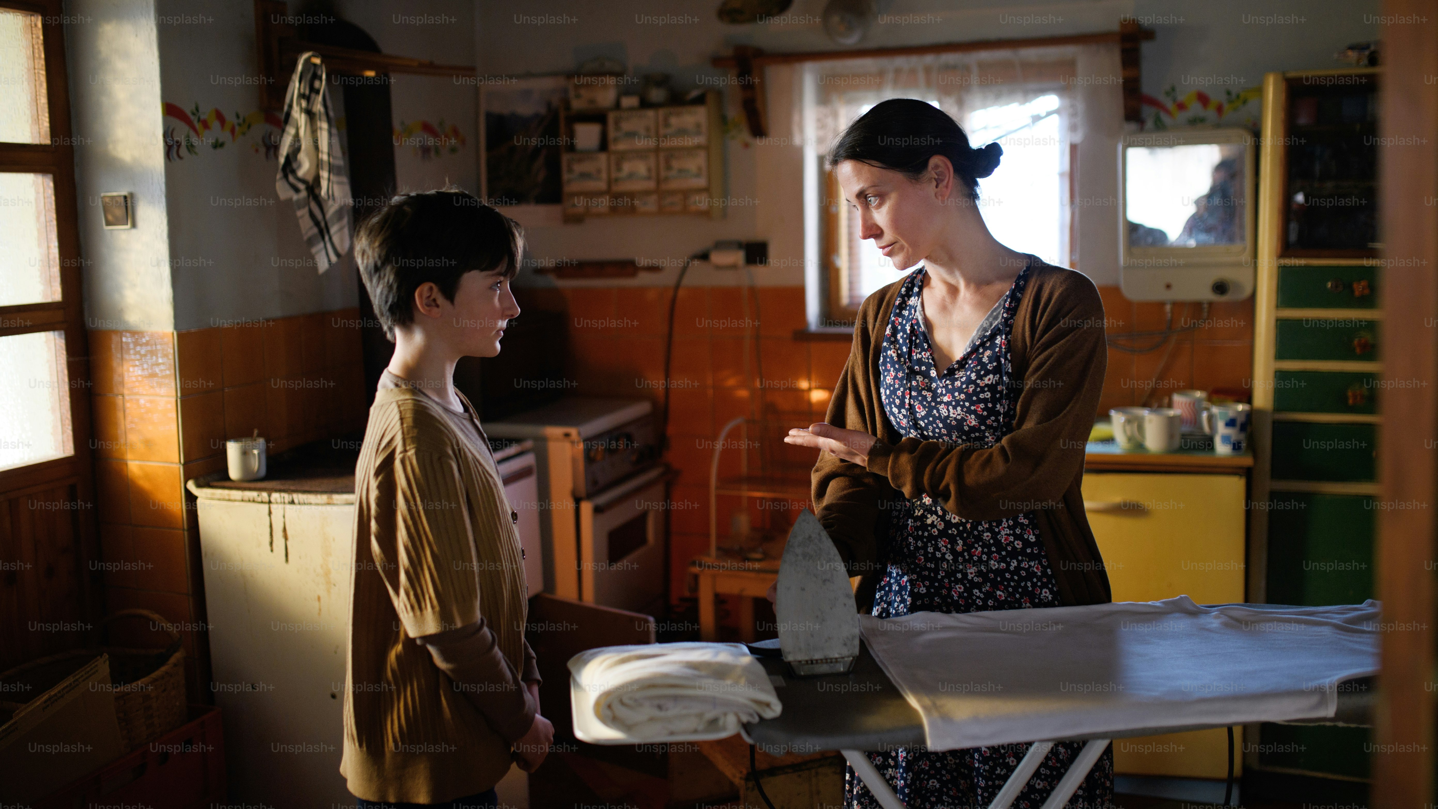 Un ritratto di una madre povera e matura triste che parla con la figlia piccola in casa a casa, concetto di povertà.