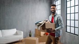 Un joven feliz sosteniendo cajas de embalaje que se mudan a casa, mirando a la cámara, un nuevo concepto de vida.