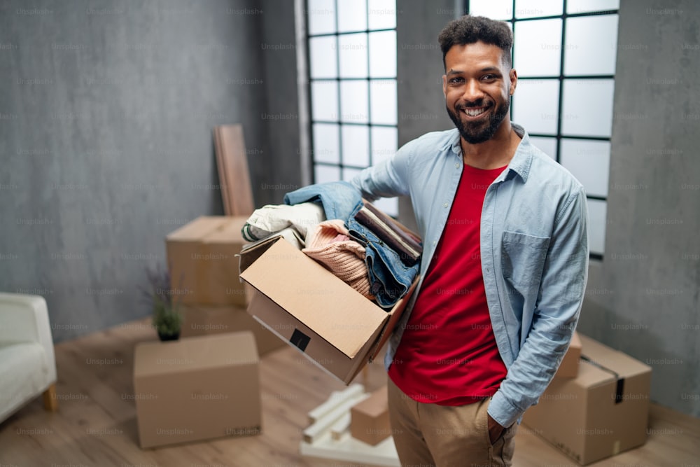 A happy young man holding packing boxes moving home, looking at camera, new living concept.