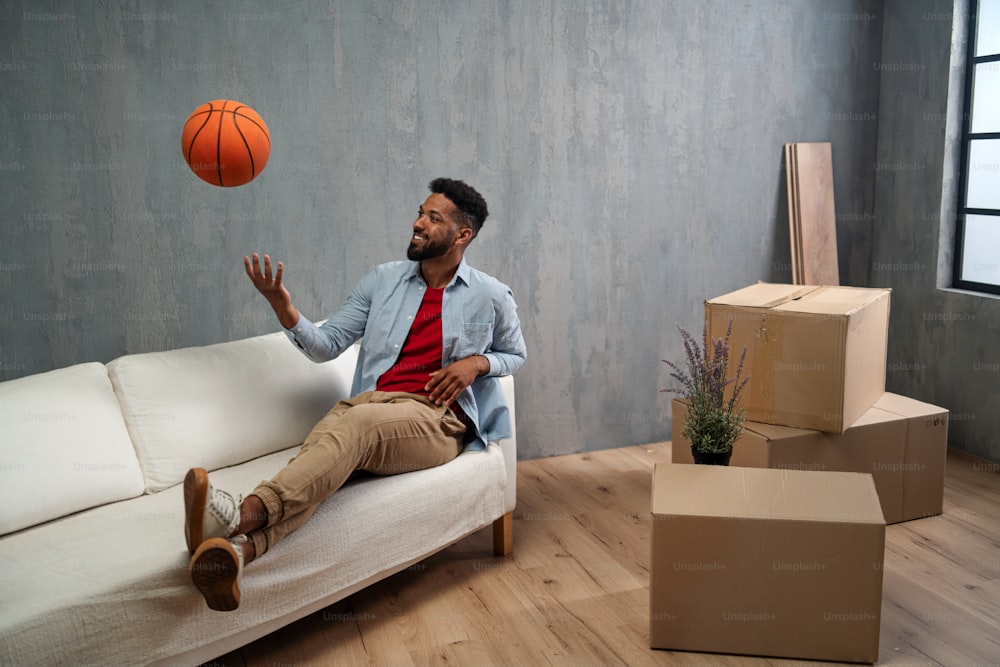 Um jovem feliz sentado no sofá e brincando com baskteball, novo conceito de vida.