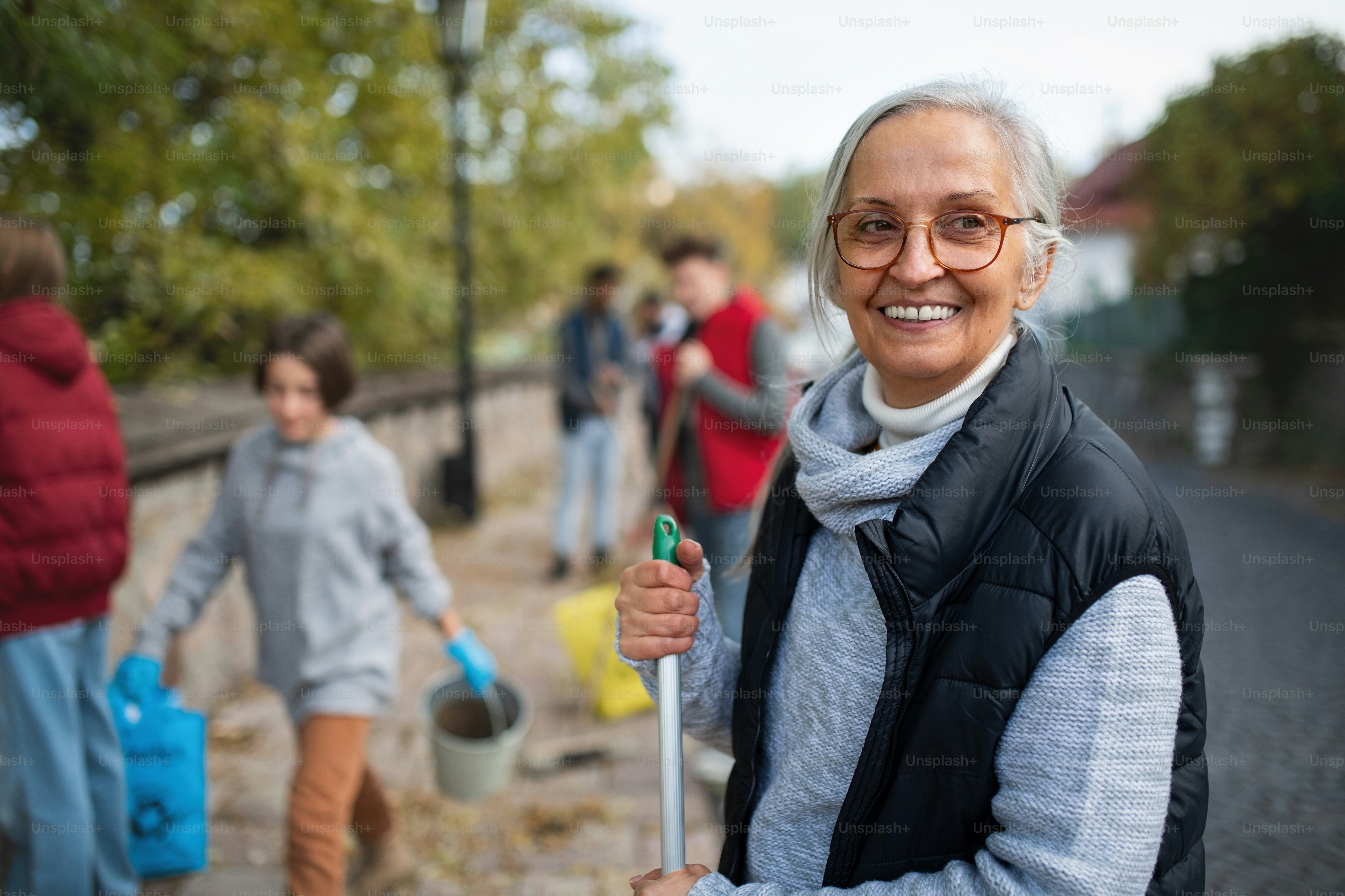 Happy senior woman volunteer with team cleaning up street, community service concept