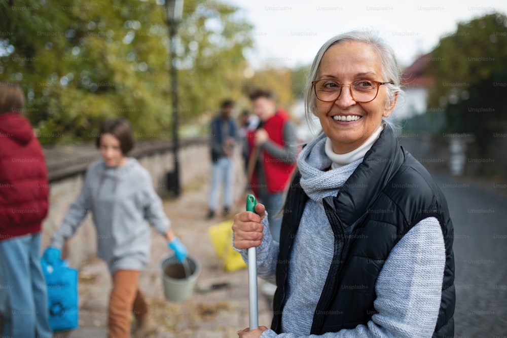 Glückliche Seniorin, ehrenamtliche Helferin mit Team, das die Straße aufräumt, gemeinnütziges Konzept