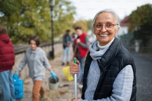 Happy senior woman volunteer with team cleaning up street, community service concept