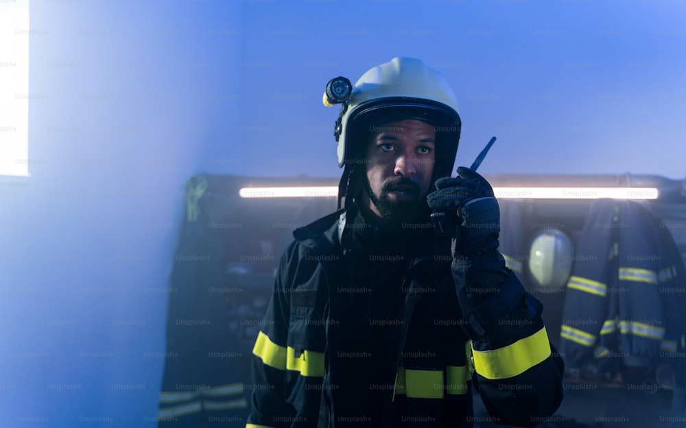 A young African-American firefighter talking to walkie talkie in fire station at night.