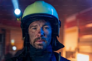 A portrait of dirty firefighter man on duty with fire truck in background at night, looking at camera.