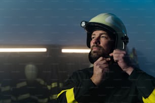 A mature firefighter preparing for action in fire station at night, looking at camera.