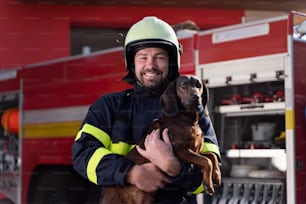 犬を持ち、消防車を背景にカメラを見る幸せな成熟した消防士の男性