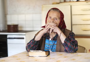 Sehr alte Frau mit Kopftuch betet in ihrer Küche im Landhausstil