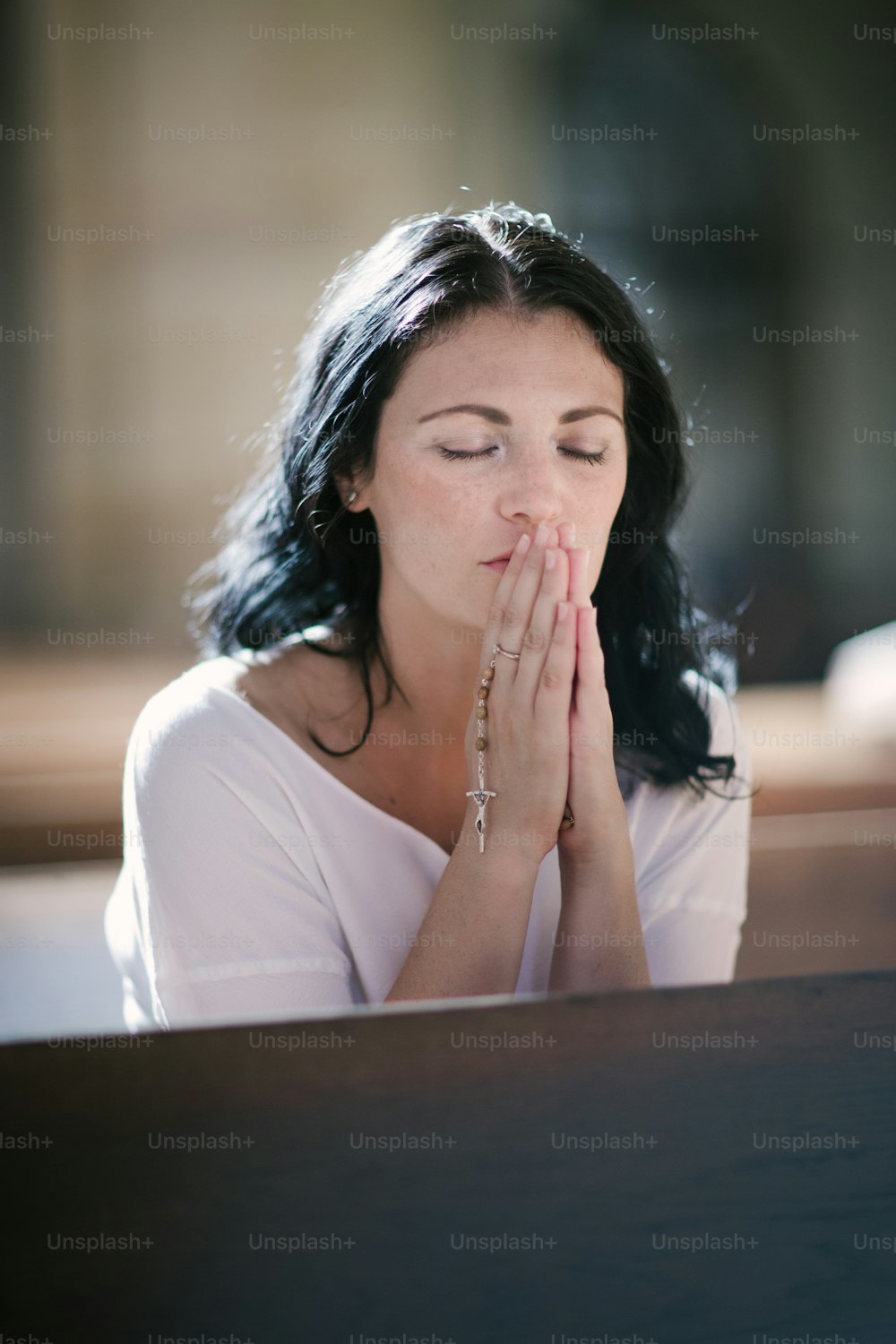 教会で祈るロザリオを持つ美しい女性