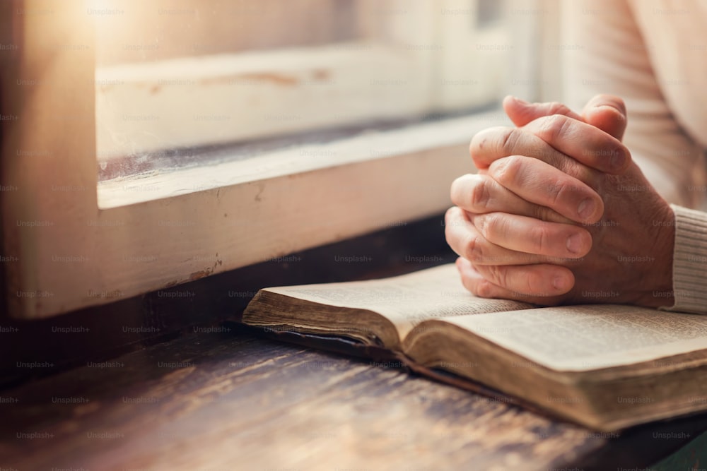 Mãos de uma mulher irreconhecível com a Bíblia orando