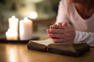 Una anciana irreconocible yacía en el suelo orando con las manos juntas sobre su Biblia. Encendiendo velas a su lado. Cerrar.