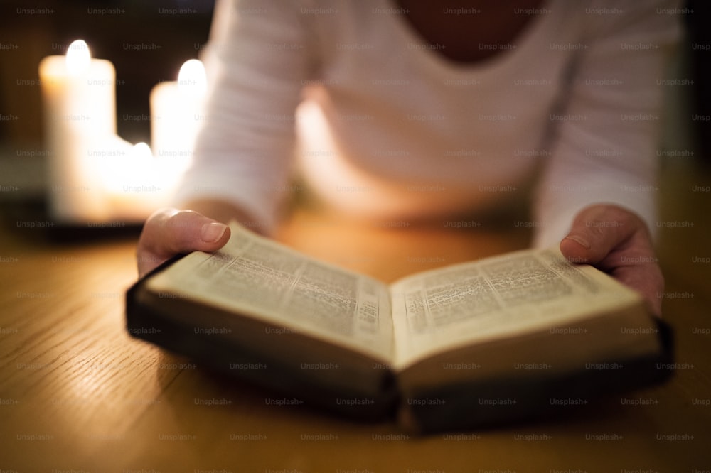 Donna anziana irriconoscibile sdraiata sul pavimento a leggere la sua Bibbia. Candele accese accanto a lei. Primo piano.