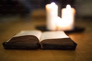 Close up de uma Bíblia antiga colocada no chão de madeira, queimando velas ao lado dela