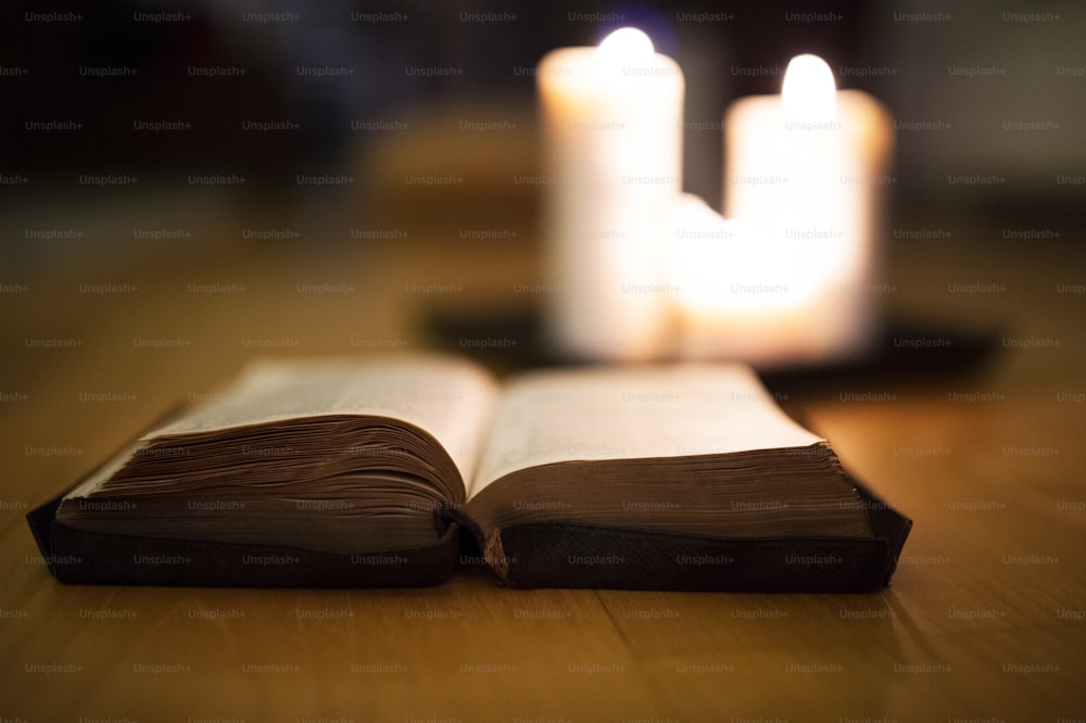 Nahaufnahme einer alten Bibel, die auf Holzboden liegt und daneben brennende Kerzen verbrennt