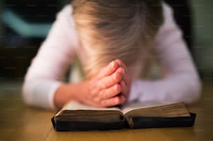 Mulher irreconhecível orando com as mãos entrelaçadas em sua Bíblia. De perto.
