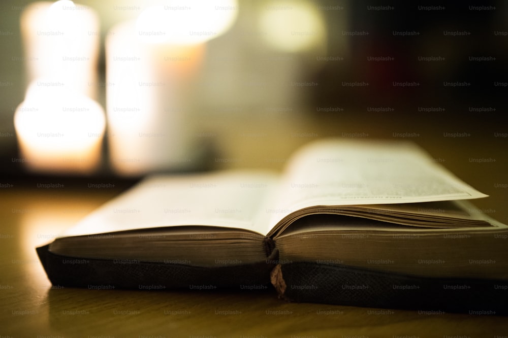 Close up of an old Bible laid on wooden floor, burning candles in the background