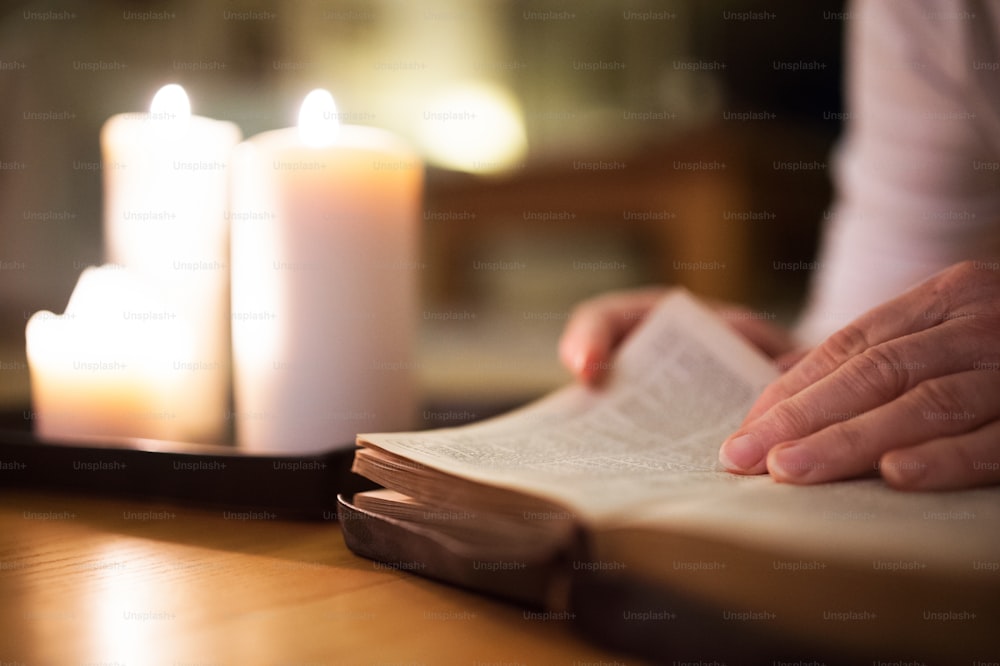 Mujer irreconocible tirada en el suelo leyendo su Biblia. Velas encendidas junto a ella. Primer plano del libro y su mano.