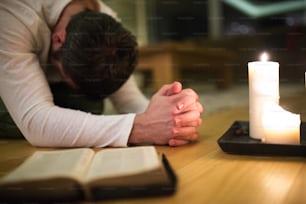 Unkenntlicher junger Mann, der betet, auf dem Boden kniet, die Hände ineinander verschränkt. Bibel und brennende Kerzen neben ihm. Aufschließen.
