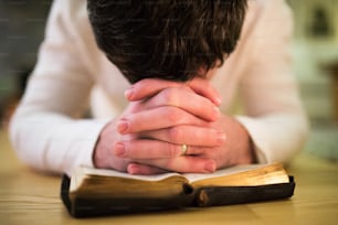 알아볼 수 없는 젊은이가 기도하고, 바닥에 무릎을 꿇고, 성경을 손에 얹고 있다. 닫다.