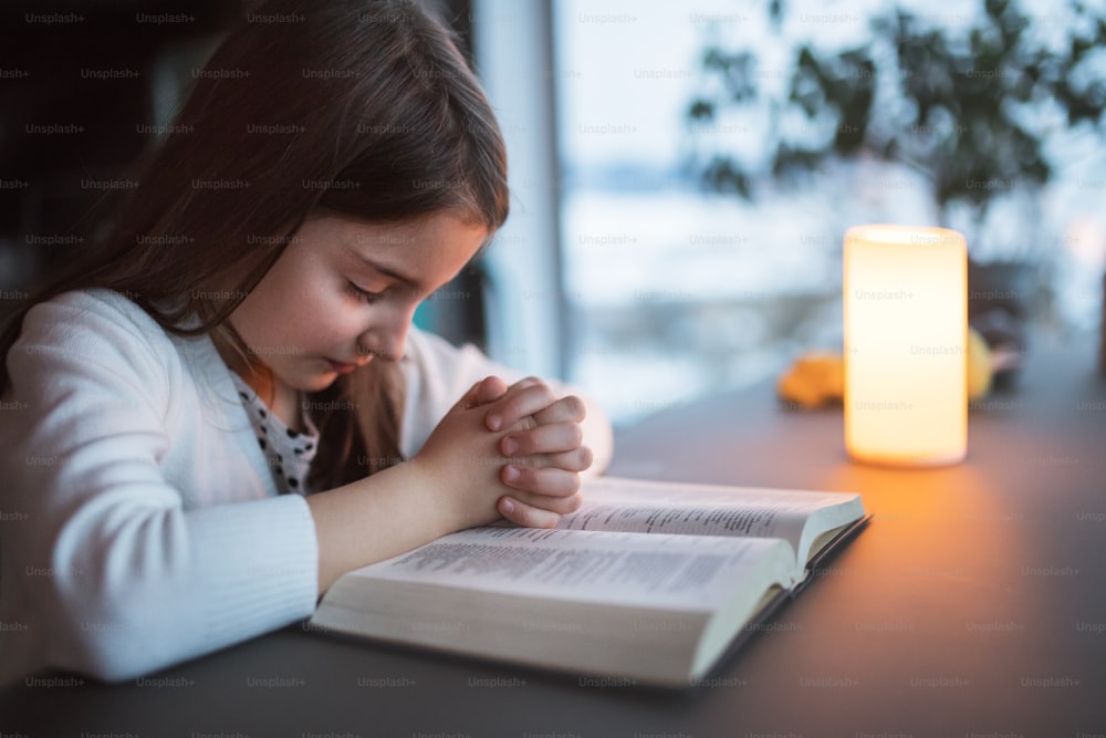 Una bambina con la Bibbia a casa, pregando.
