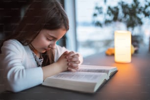 Una niña pequeña con la Biblia en casa, orando.