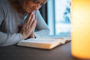 Uma mulher idosa irreconhecível orando em casa.
