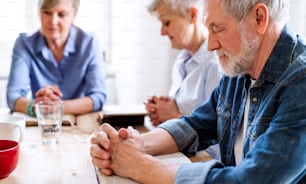 Senior people in bible reading group in community center club, praying.