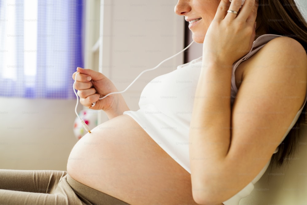 Gros plan d’une femme enceinte méconnaissable tenant l’écoute de son bébé