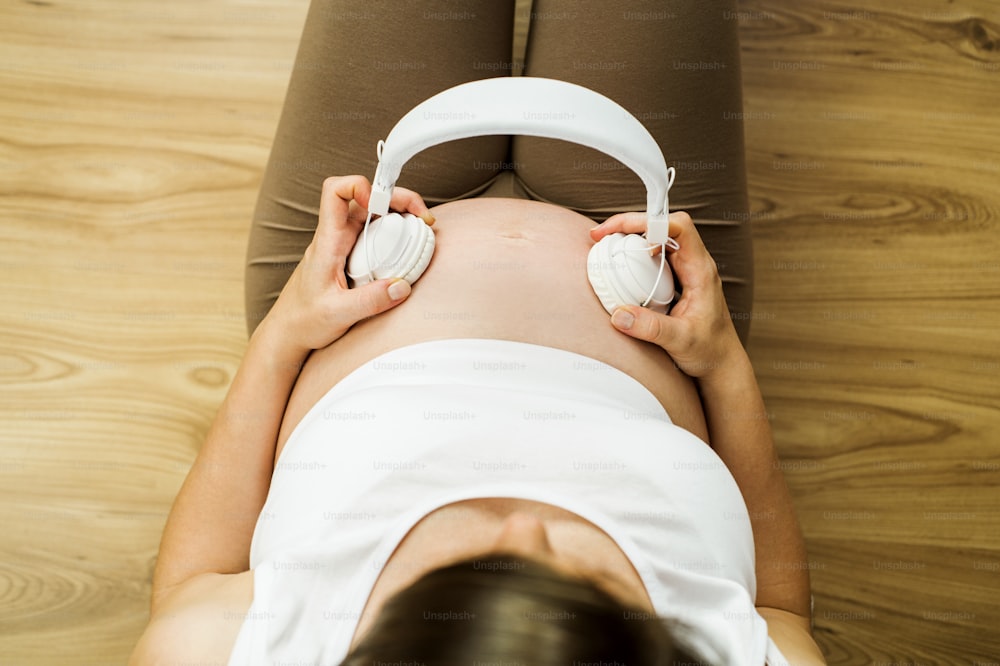Mulher grávida bonita segurando fones de ouvido sobre sua barriga