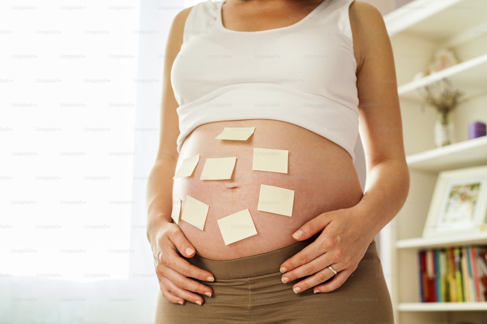 Close-up de mulher grávida irreconhecível com notas adesivas de espaço de cópia em sua barriga