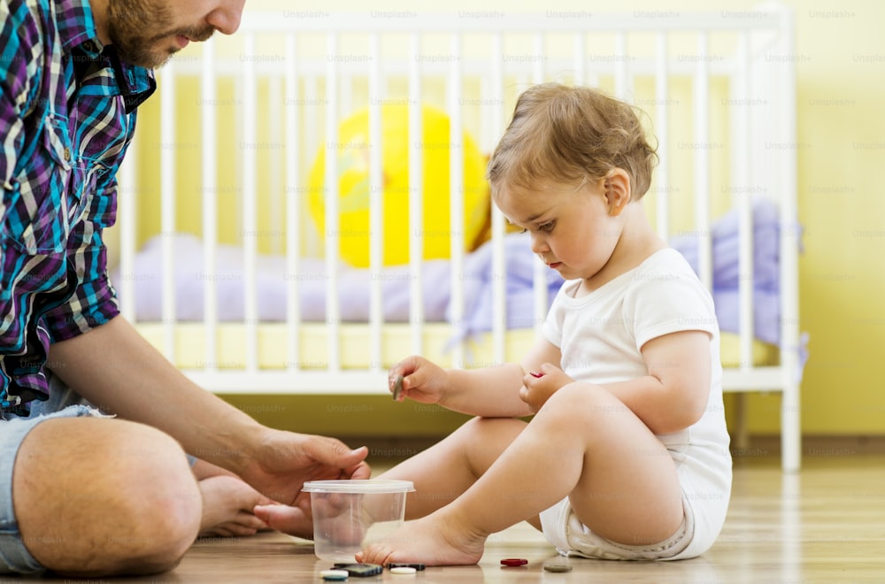 Glücklicher Vater und seine kleine Tochter spielen zu Hause mit verschiedenen Knöpfen