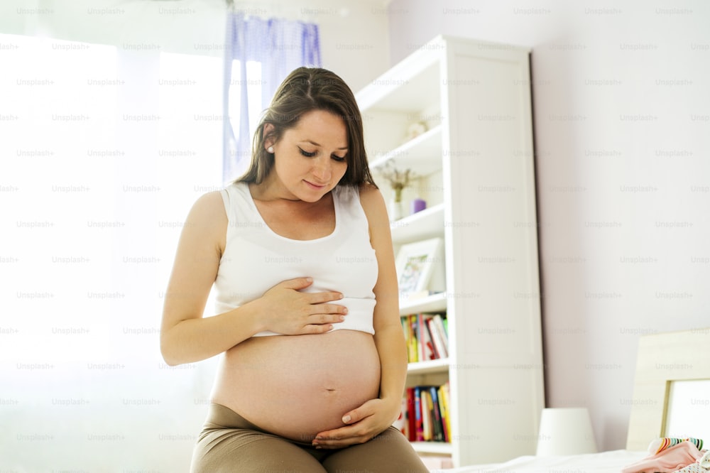 Portrait of beautiful pregnant woman holding her belly in bedroom