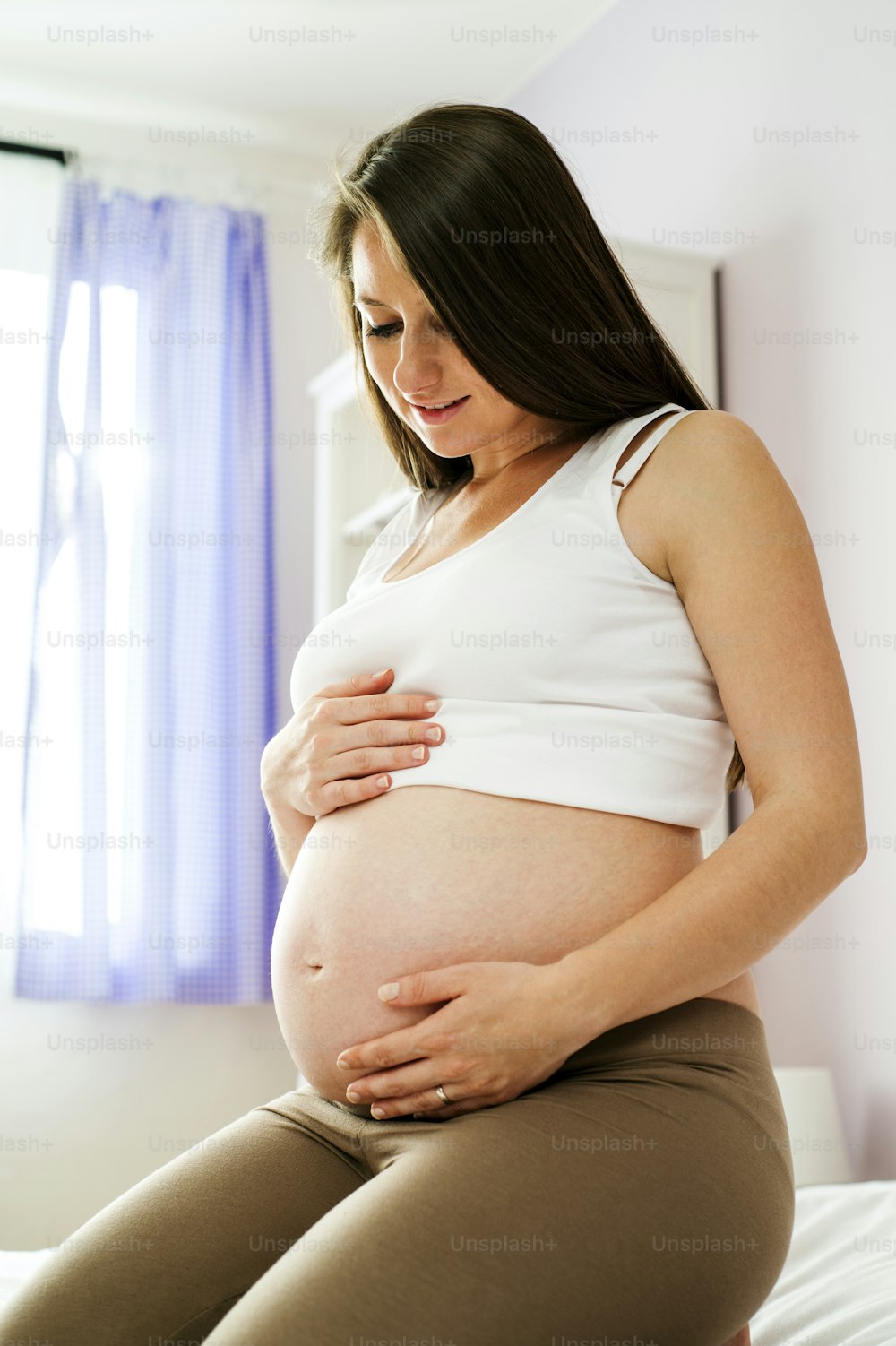 Retrato da mulher grávida bonita que segura sua barriga no quarto