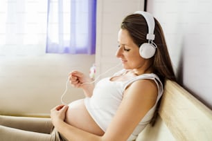 Beautiful pregnant woman listening to her baby with headphones