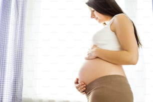 Porträt einer schönen schwangeren Frau, die ihren Bauch im Schlafzimmer hält