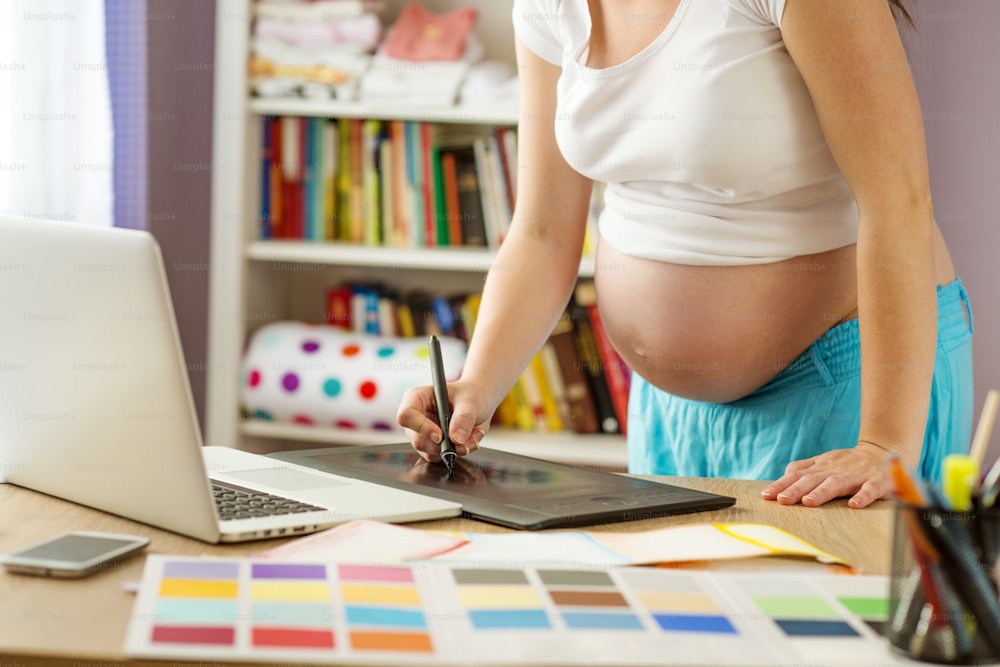Unrecognizable pregnant woman in home office with laptop
