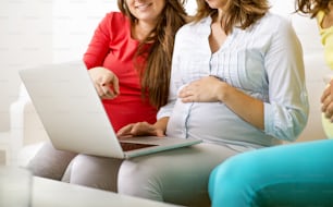 Três mulheres grávidas irreconhecíveis sentadas no sofá, conversando e usando laptop