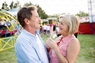 Senior couple having a good time at the fun fair, hugging. Woman holding lollipop.